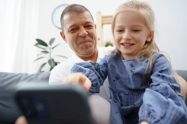 Grootvader en kleindochter kijken thuis iets op smartphone — Stockfoto