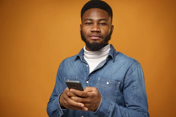 Sarı arka planda akıllı telefonunu kullanan Afrikalı Amerikalı genç bir adamın portresi. — Stok fotoğraf