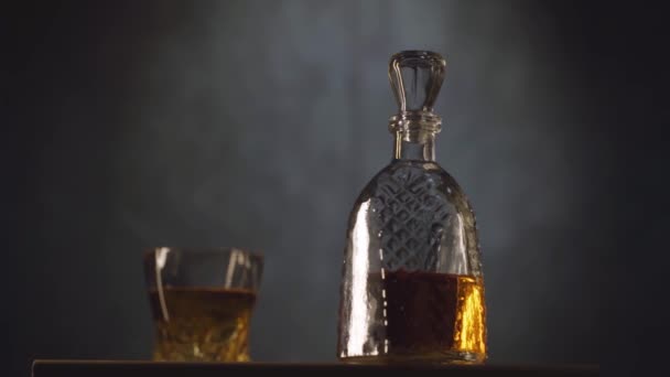 Whiskey glas en fles op tafel tegen donkergrijze achtergrond — Stockvideo