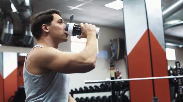 Ung man idrottsman dricksvatten från shaker flaska i gymmet — Stockvideo