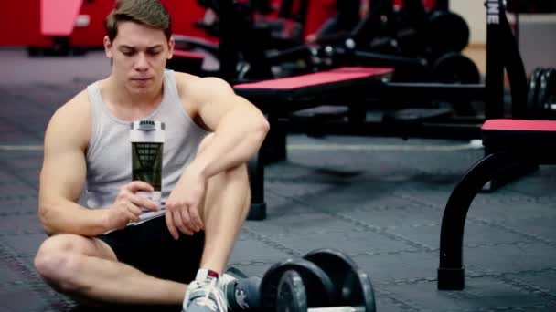 Ung man idrottsman dricksvatten från shaker flaska i gymmet — Stockvideo