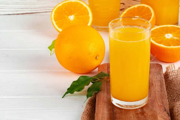 Glass of orange juice and cut oranges on table — Stock Photo, Image