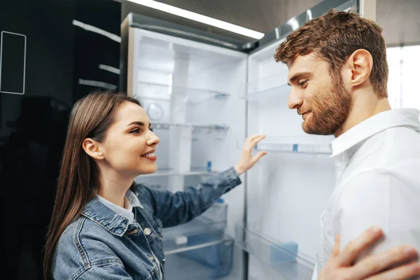 Jovem casal selecionando novo refrigerador na loja de eletrodomésticos — Fotografia de Stock