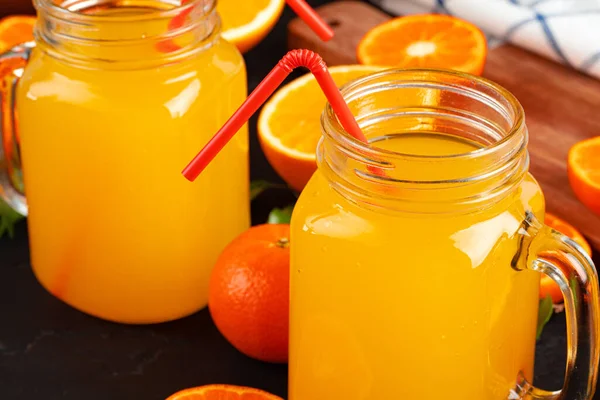 Glass of orange juice and cut oranges on table — Stock Photo, Image