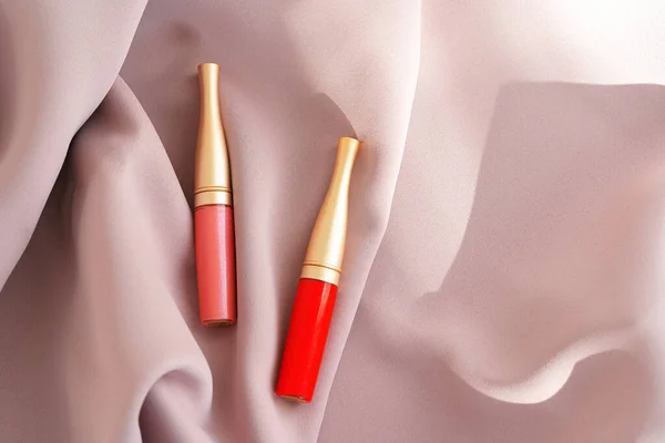 Los productos de maquillaje de brillo labial en tela sedosa rosa — Foto de Stock