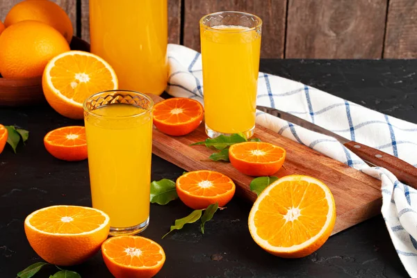 Glass of orange juice and cut oranges on table — Stock Photo, Image