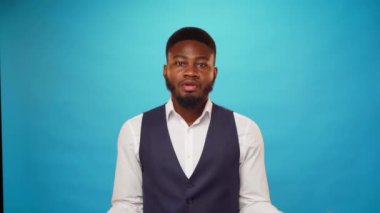 Genç Afrikalı Amerikalı iş adamı mavi arka plana karşı duruyor, üzerine dolar banknotları düşüyor.