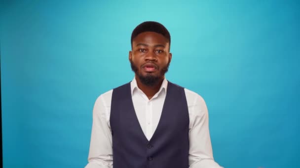 Молодий афроамериканець, який стоїть навпроти синього фону, доларові купюри падають на нього. — стокове відео