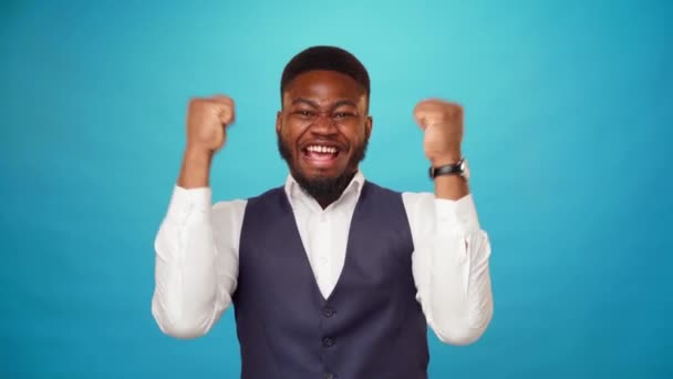 Radostný šťastný mladý africký Američan chlap slaví úspěch, je vítěz, modré pozadí — Stock video