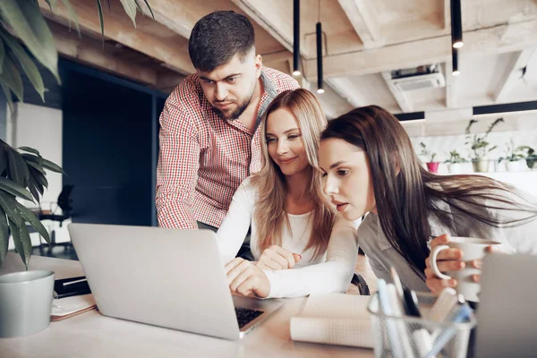 Två kvinnliga och en manlig affärspartner tittar på datorskärmen och diskuterar sitt projekt — Stockfoto