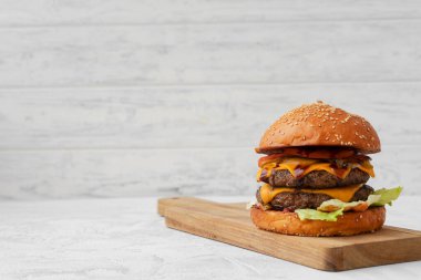 Tahtada beyaz bulanık arka plana karşı duble çizburger servis ediliyor.