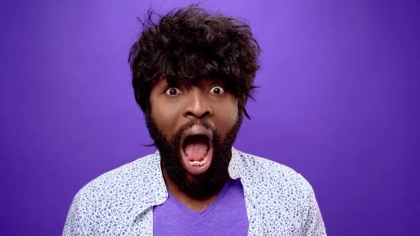 Šokovaný ohromený mladý vousatý černošky afroameričan muž, fialové pozadí — Stock video