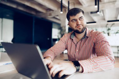 Gündelik gömlekli genç adam ofiste bilgisayarla çalışıyor.