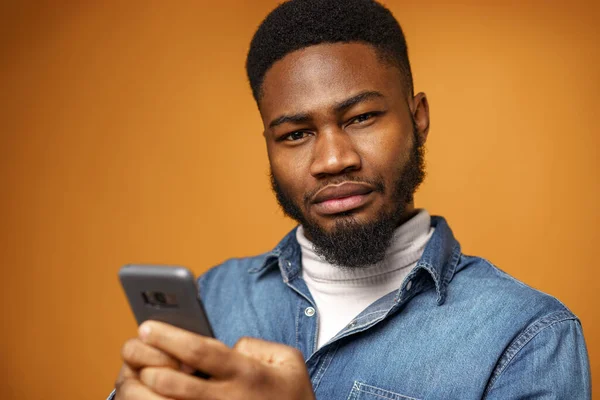 Sarı arka planda akıllı telefonunu kullanan Afrikalı Amerikalı genç bir adamın portresi. — Stok fotoğraf