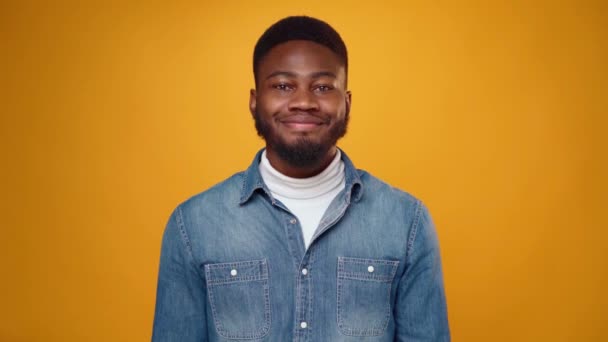 Удивлённый молодой африканский мужчина показывает большие пальцы на жёлтом фоне в студии — стоковое видео