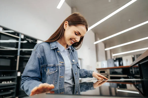 Ung brunett kvinna väljer ny elektrisk spis i en stormarknad — Stockfoto