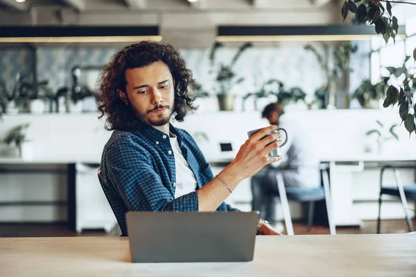 Ung affärsman använder laptop och håller en kopp kaffe på kontoret — Stockfoto