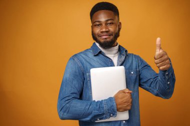 Sarı arka planda dizüstü bilgisayarı olan genç bir Afro-Amerikan.