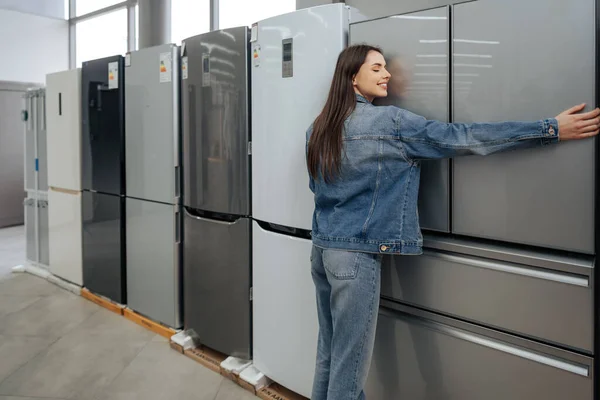 Joven mujer feliz apoyada en su nuevo refrigerador en un centro comercial — Foto de Stock