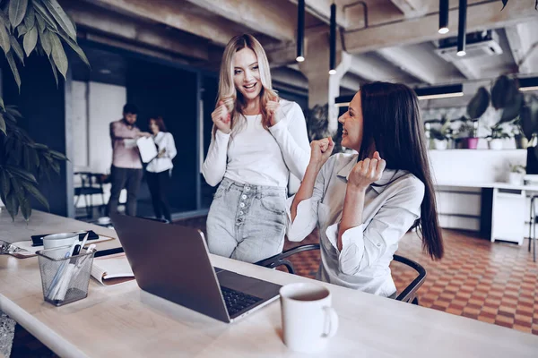 Duas jovens empresárias felizes comemorando o sucesso do projeto no escritório — Fotografia de Stock