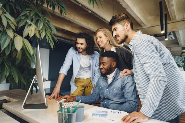 Vier multiethnische Kollegen blicken im Büro auf Computerbildschirm — Stockfoto