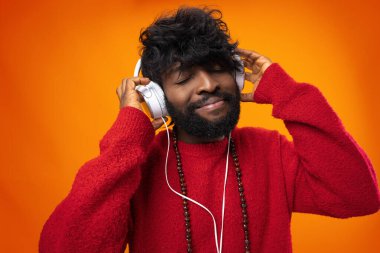 Afrikalı Amerikalı adam turuncu arka planda neşe içinde müzik dinliyor.