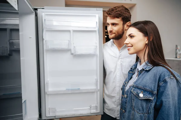 Pareja joven seleccionando nuevo refrigerador en la tienda de electrodomésticos — Foto de Stock