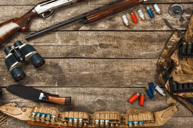 Tüfek, bıçak, dürbün ve fişekler de dahil olmak üzere eski ahşap arka planda avlanma ekipmanları.