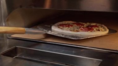 Şef yeni yapılmış pizzayı yuvarlak kesiciyle kesiyor.