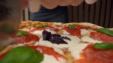 Şef yeni yapılmış pizzayı yuvarlak kesiciyle kesiyor.