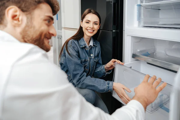 Jovem casal selecionando novo refrigerador na loja de eletrodomésticos — Fotografia de Stock