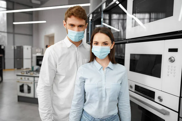Fiatal pár orvosi maszkot visel a hipermarketben háztartási készülékekkel — Stock Fotó