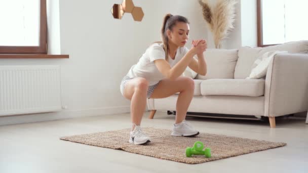 Mulher desportiva faz agachamentos em um quarto, exercícios de aptidão em casa — Vídeo de Stock