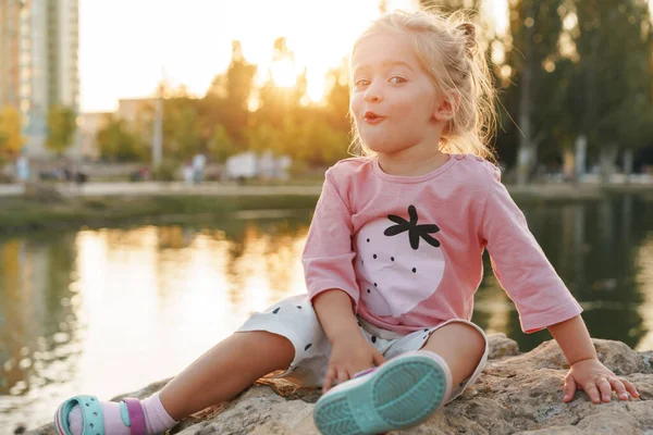 Petite fille assise sur une énorme pierre dans le parc près du lac — Photo
