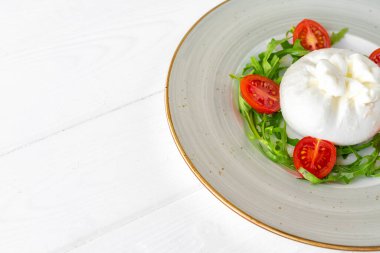 Burrata peynirli salata ve beyaz ahşap arka planda vişneli domates.