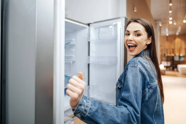 Jovem mulher atraente escolhendo geladeira no hipermercado — Fotografia de Stock