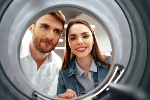 Pareja feliz eligiendo la nueva lavadora en una tienda, vista desde el interior de la lavadora — Foto de Stock