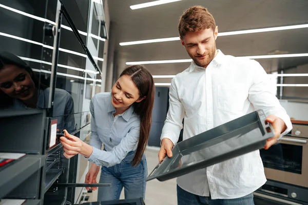 Pareja joven eligiendo nuevo horno eléctrico en hipermercado — Foto de Stock