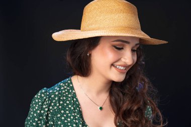Hasır şapkalı, siyah arka planda poz veren güzel bir genç kadın.