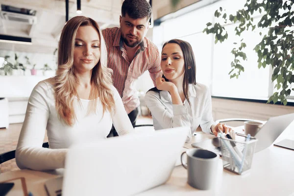 Två kvinnliga och en manlig affärspartner tittar på datorskärmen och diskuterar sitt projekt — Stockfoto