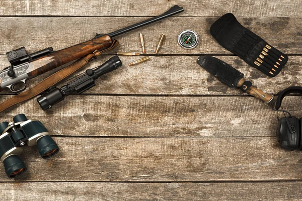 Lovecké vybavení na starém dřevěném pozadí včetně pušky, nože, dalekohledu a nábojů — Stock fotografie