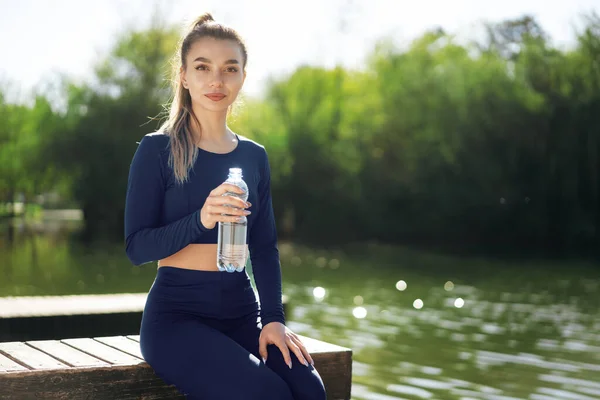 Πορτρέτο της νεαρής όμορφης γυναίκας φορώντας μπλε αθλητικά ρούχα πόσιμο νερό στο πάρκο — Φωτογραφία Αρχείου