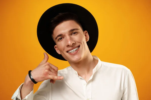 Young man in black hat showing call me sign against yellow backgorund — Stock Photo, Image