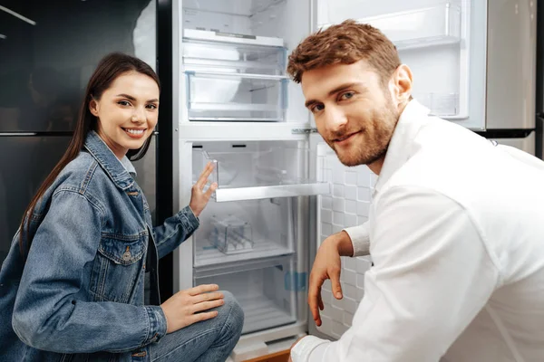 Jovem casal selecionando novo refrigerador na loja de eletrodomésticos — Fotografia de Stock