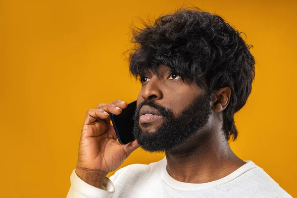 Sarı arka planda cep telefonuyla konuşan genç bir Afrikalı. — Stok fotoğraf