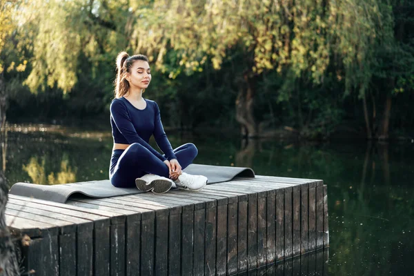 Молода жінка на килимку для йоги, що розслабляє на відкритому повітрі — стокове фото