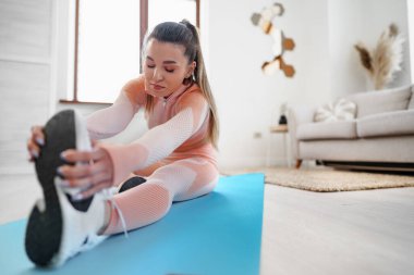 Genç ve formda bir kadın evde esneme hareketleri yapıyor.