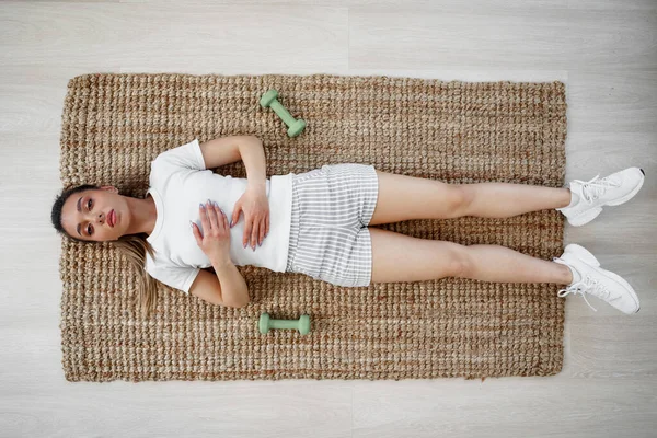 Vista superior de una chica en forma joven haciendo ejercicio en una alfombra en casa — Foto de Stock