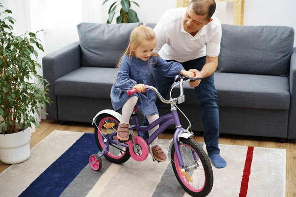 Grandpa teaching his granddaughter riding a bicycle at home — Foto de Stock