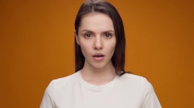 Sessiz olmak için el sallayan, sarı arka plana karşı sessizlik dilenen genç bir kadına yaklaş.